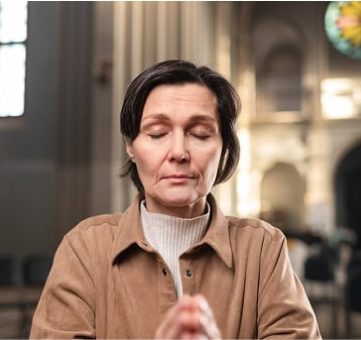 Woman praying with eyes closed in a church setting.