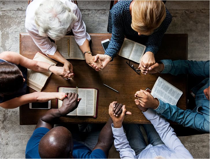 Diverse group of people holding hands over a table with books and tablets.
