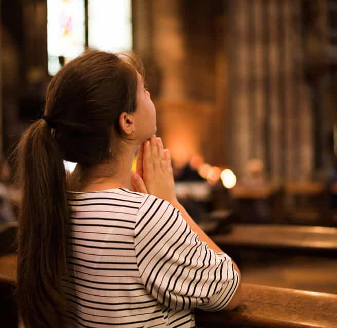 Woman praying in a church with hands clasped, facing altar, peaceful atmosphere.