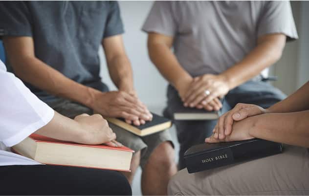Group of people holding religious books during a discussion or study session.