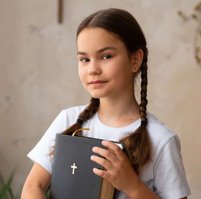 Young girl holding a religious book with a cross, indoors.