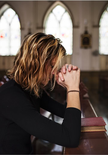 A woman praying with her hands clasped in a church setting.