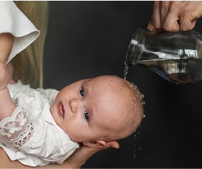 A baby receiving a traditional baptismal blessing with water poured over their head.