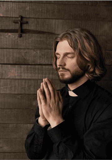Young man praying with hands together in a wooden church setting.