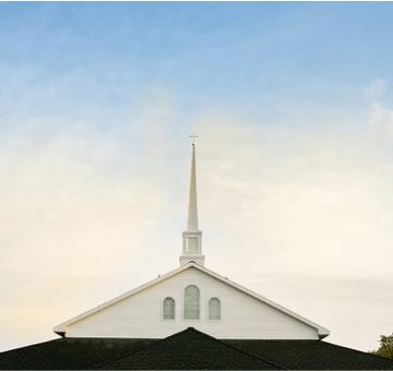 A church steeple with a cross on top against a partly cloudy sky.